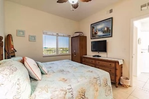 A bedroom with a bed, a dresser, a television, and a window with a view.