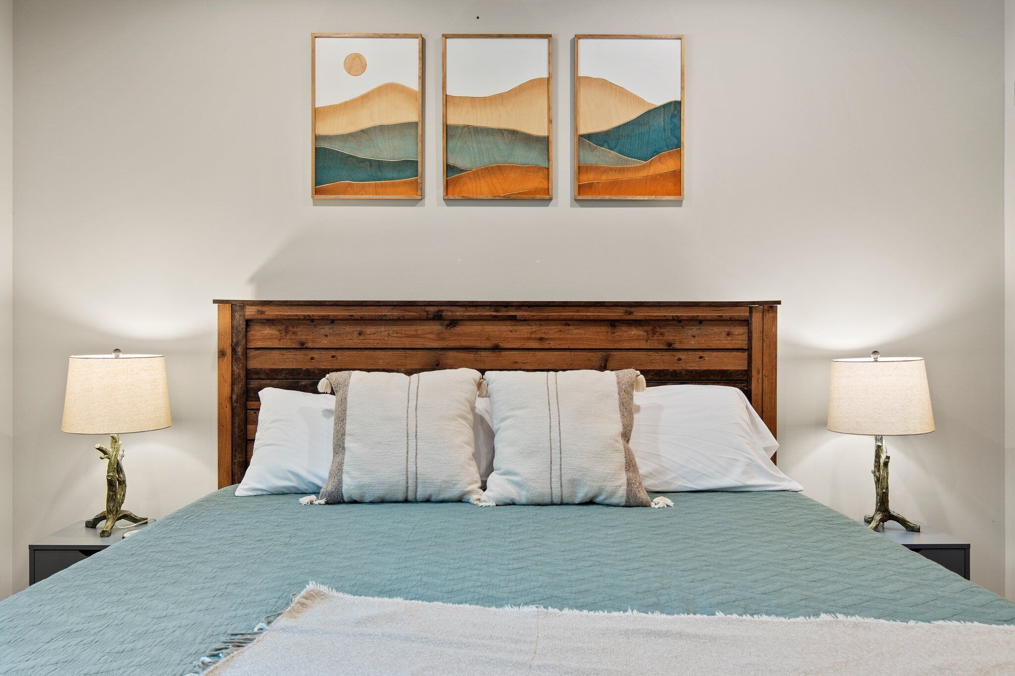 Une chambre à coucher avec une tête de lit en bois, deux lampes de chevet, un lit recouvert d’une courtepointe bleue et trois tableaux accrochés au mur.