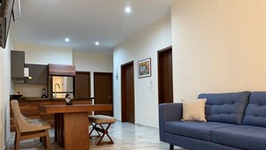 A modern living room with a blue sofa, a wooden dining table, and a kitchen area with a built-in oven and cabinets. - New 3-Bedrooms apartment close to the beach. (Mazatlan)