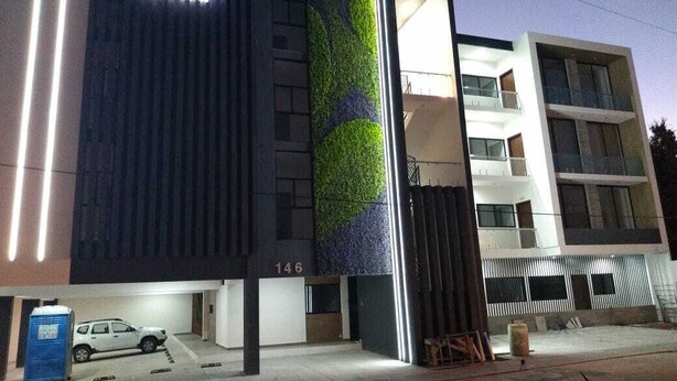 A modern building with a prominent 'CERM' sign, a green vertical garden, and a parking area with a white car and portable toilets. - New 3-Bedrooms apartment close to the beach. (Mazatlan)