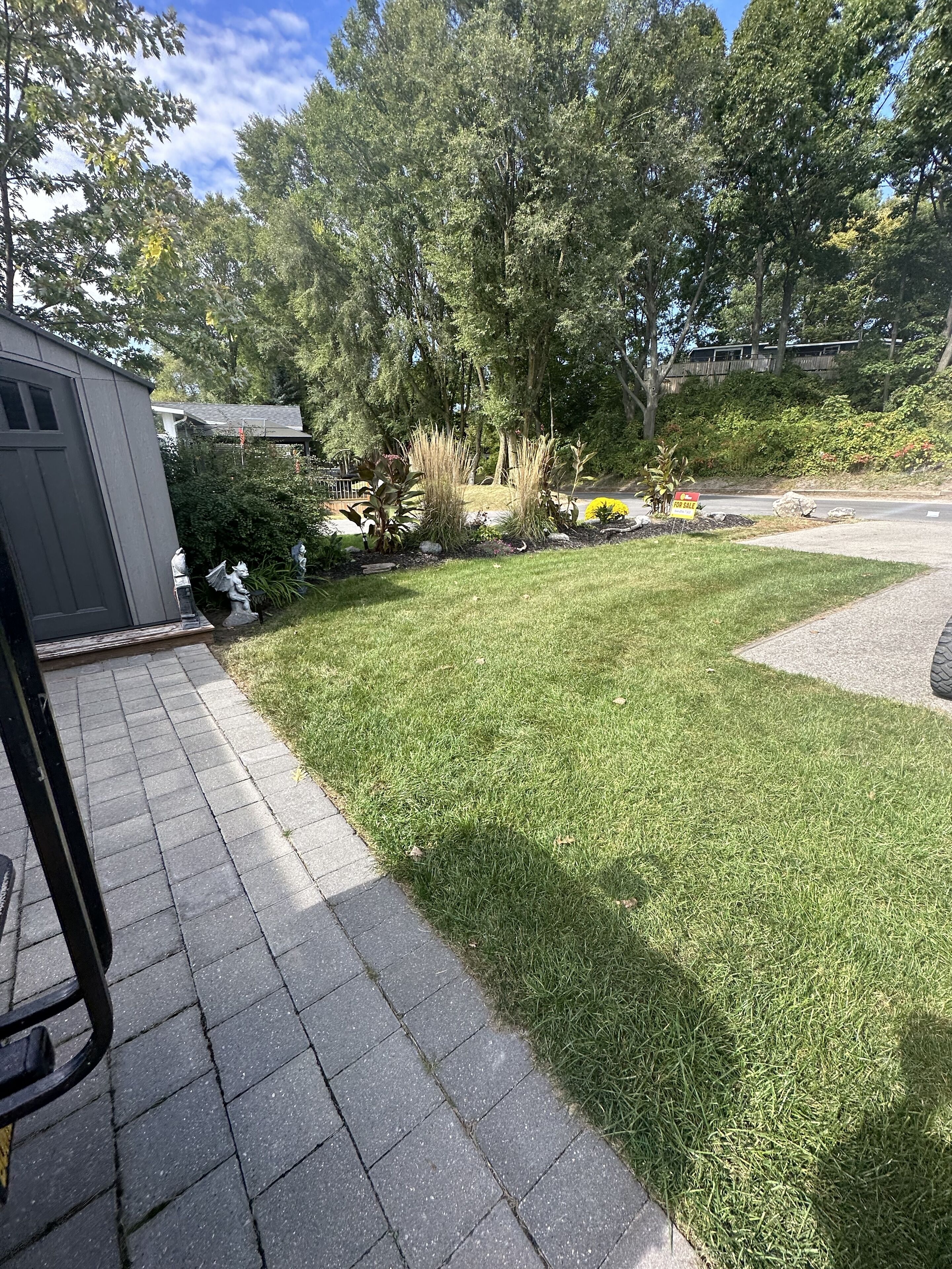 Ein Wohnweg mit gepflegtem Rasen, einer kleinen Gartenhütte und verschiedenen Pflanzen und Sträuchern.