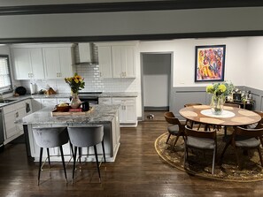 A modern kitchen with white cabinets, a marble island, and a dining area with a round table and chairs. - Spacious home with spacious backyard ! (Atlanta)