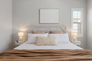 A neatly arranged bedroom with a bed, two bedside tables, a wall-mounted picture, and a window with blinds.