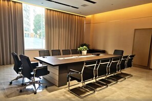 Una sala de conferències amb una taula llarga, cadires negres i una planta en test.