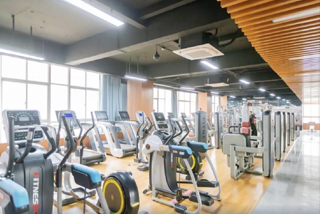 A gym with various exercise machines, large windows, and a wooden ceiling.