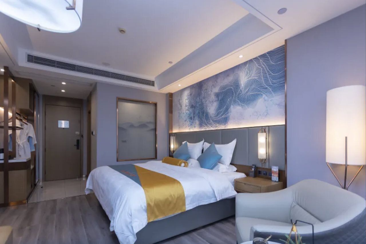 A modern hotel room with a large bed, bedside tables, a seating area, and a large abstract artwork on the wall.