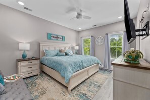 A bedroom with a bed, nightstands, a dresser, a ceiling fan, and a window with curtains.