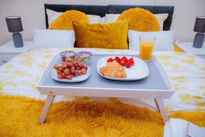 A neatly made bed with a tray table holding a breakfast tray with grapes, strawberries, and a croissant, along with a glass of orange juice. - Beautiful two bedrooms ensuite apartment (Northampton)