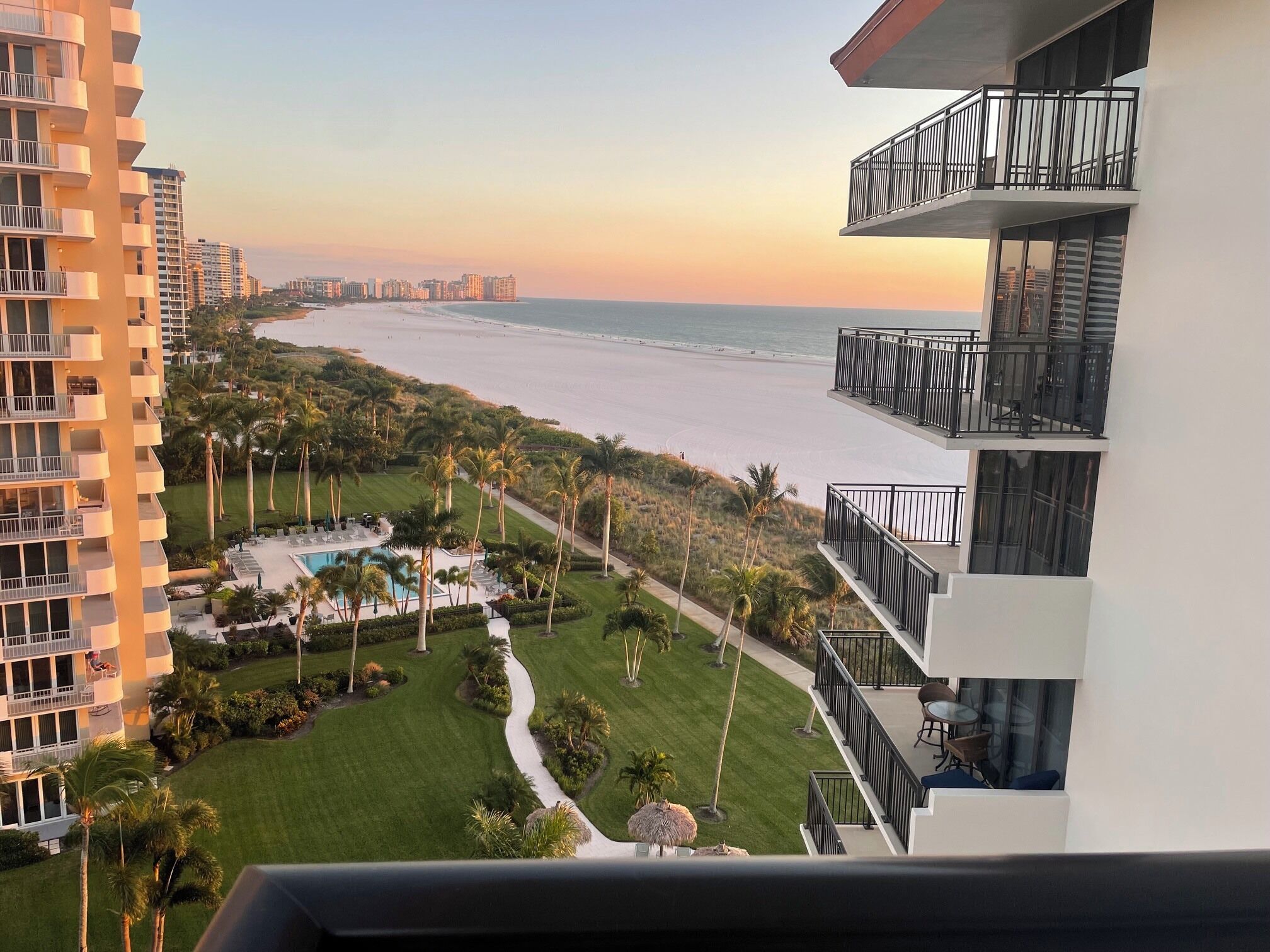A high-rise hotel with multiple balconies overlooking a beach and a pool area.