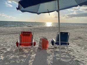 Two beach chairs under a checkered umbrella on a sandy beach with the ocean in the background. - Beautifully remodeled condo offering breathtaking Gulf views right on the beach. (Marco Island)