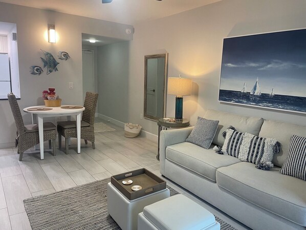 Una sala de estar moderna con un sofá, una mesa de comedor con sillas, una mesa de centro y un cuadro grande en la pared.