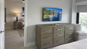 Une chambre moderne dotée d’un grand téléviseur diffusant un paysage magnifique, d’une commode en bois et offrant une vue sur l’extérieur.