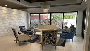 Un salon spacieux au design moderne, comprenant un canapé beige, des fauteuils bleus et une table basse à motifs.