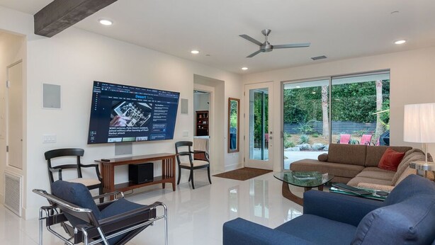 A spacious living room with a large TV, comfortable seating, and a glass door leading to a garden.