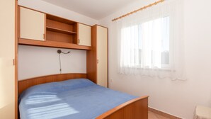 A bedroom with a bed, wooden wardrobe, and a window with sheer curtains.