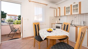 A compact kitchen with a dining area, a small window with sheer curtains, and a view of the outside.