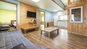 Una habitación compacta con cama, un banco de madera, una mesita pequeña, televisión y kitchenette.
