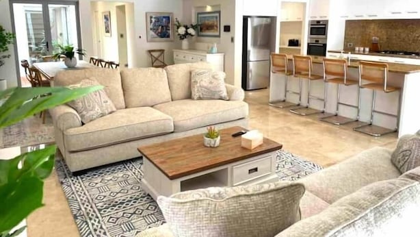 Een moderne woonkamer met een bank, salontafel en een keukenhoek met barstoelen.