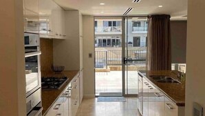 Een moderne keuken met witte kasten, een ingebouwde oven en een groot raam met uitzicht op een balkon.