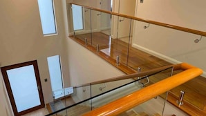 Een modern interieur met glazen balustrade, houten vloer en uitzicht op een verdieping lager.