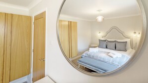 Une chambre avec un miroir rond, une armoire en bois et un lit avec des oreillers et une couverture.