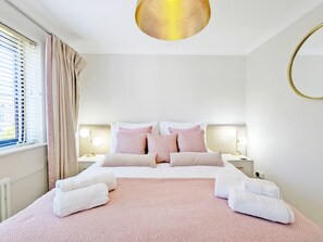 Ein ordentlich bezogenes Bett mit rosa Bettwäsche, zwei Nachttischlampen und ein runder Spiegel an der Wand.