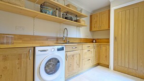 Une cuisine compacte avec des meubles en bois, un lave-linge Bosch et des paniers en osier placés sur des étagères.