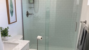 Ett modernt badrum med en dusch som är avskärmad med glasväggar, en vit marmorhandfat och en toalett.