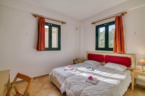 A bedroom with two beds, a wooden chair, a nightstand, and a window with curtains. - Analipsi Villas Beach Front 5, Kastro Kyllini, Greece (Kastro Kyllini)