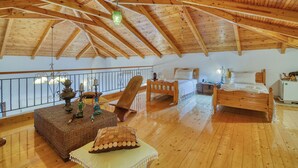 A spacious loft bedroom with a high wooden ceiling, a bed, a chair, and a small table with decorative items.