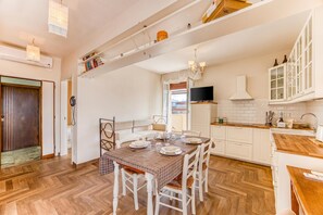 Een eetgedeelte met een tafel voor vier personen, witte stoelen, een houten visgraatvloer, en een keuken met witte kasten en een houten aanrecht.