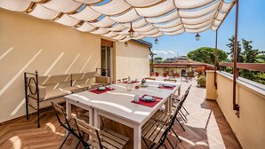 An outdoor dining area with a white table and chairs, a covered seating area, and a view of the cityscape. - Terrazza Apuana A Few Steps From The Sea, Forte dei Marmi, Italy (Forte dei Marmi)