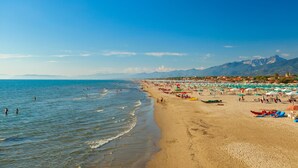 A beach with clear skies, calm waters, and a distant mountain range. - Terrazza Apuana A Few Steps From The Sea, Forte dei Marmi, Italy (Forte dei Marmi)