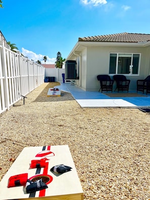 A backyard with a pool, a white fence, and a patio area with chairs.