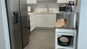 Uma cozinha com armários brancos, geladeira de aço inoxidável, micro-ondas e cafeteira.