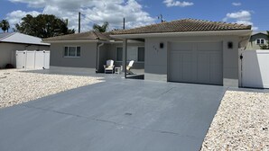 Uma casa de dois andares com garagem, varanda coberta com cadeiras e entrada por rampa.
