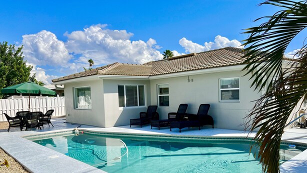 Piscina com espreguiçadeiras, mesa de pátio e cerca branca.