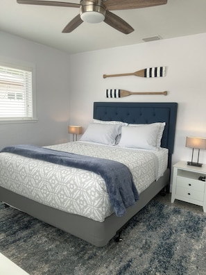 A bedroom with a bed, a ceiling fan, a nightstand, and wall-mounted paddleboards.