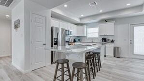 A modern kitchen with white cabinets, stainless steel appliances, and a central island with stools. - Livin' Lobster - New, Near Beach🌊🏖 , Sleeps 8, Pet Friendly🐶, 📍Central Location (Bolivar Peninsula)