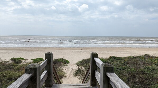 A wooden boardwalk leading to a sandy beach with the ocean in the background.