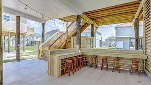 A wooden deck with a bar area and stools, a staircase, and a view of neighboring houses. - Livin' Lobster - New, Near Beach🌊🏖 , Sleeps 8, Pet Friendly🐶, 📍Central Location (Bolivar Peninsula)