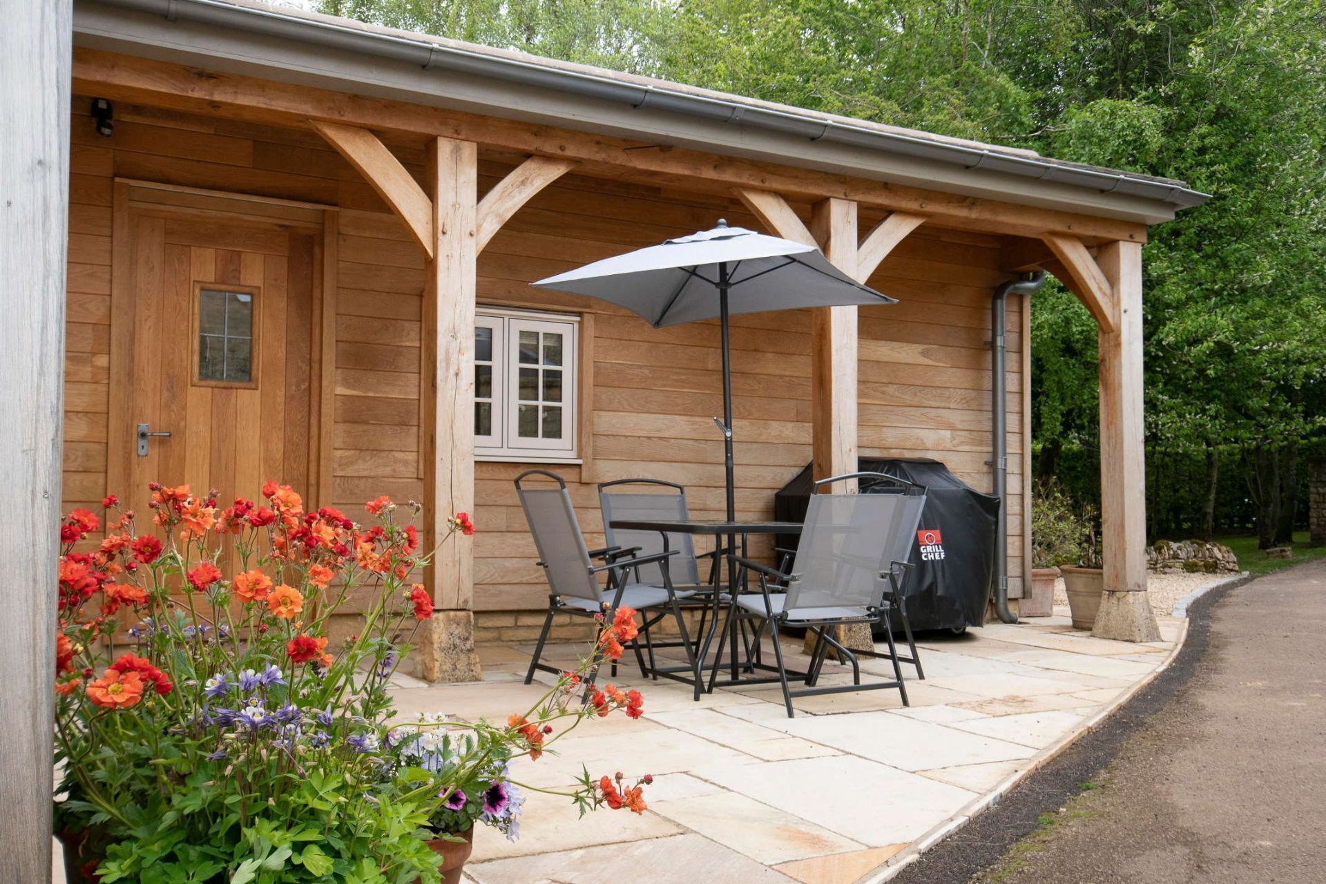 A covered patio with a table and chairs, a grill, and a flower bed.