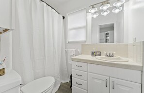 Un baño moderno con inodoro blanco, lavamanos con espejo y cortina de ducha.