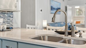 Een moderne keuken met een roestvrijstalen spoelbak, een achterwand met blauwe tegels en een schilderij aan de muur.
