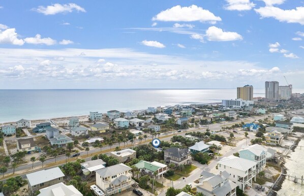 Un pueblo costero con propiedades frente a la playa, cielo despejado y una combinación de edificios residenciales y comerciales.