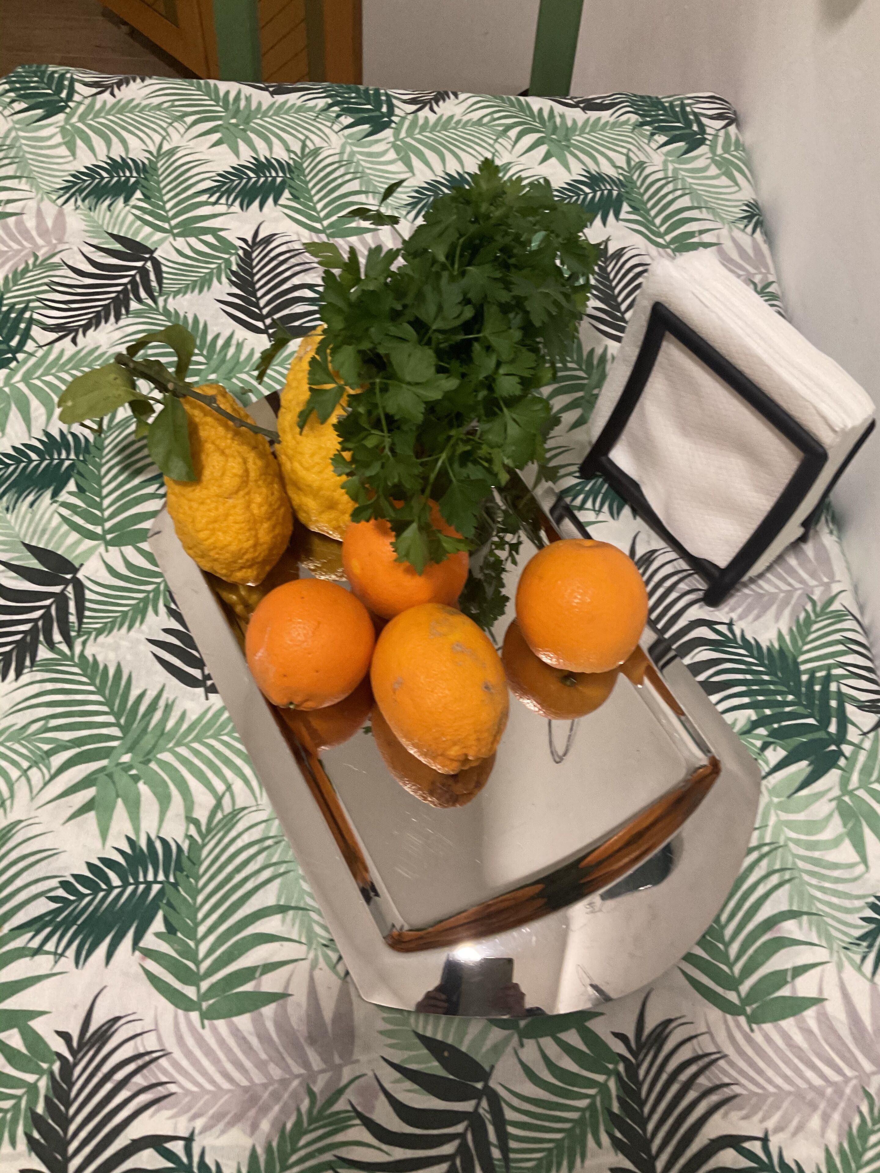 Ein Tablett mit Zitronen, Orangen und einem Zweig Petersilie auf einer Tischdecke mit Blätermuster.
