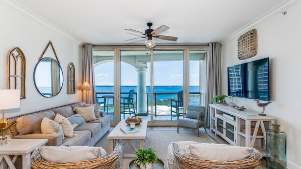 Amplia sala de estar con un gran ventanal con vista al mar, ventilador de techo y televisor.
