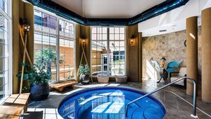 Una piscina interior con vistas al exterior, rodeada de amplios ventanales, una estatua y un banco.