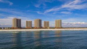 Un hotel frente a la playa con varios edificios altos, una playa de arena y un cielo azul despejado.