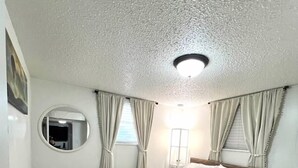Ein Schlafzimmer mit einem Bett, einem runden Spiegel, einem Nachttisch und einem Fenster mit Vorhängen.